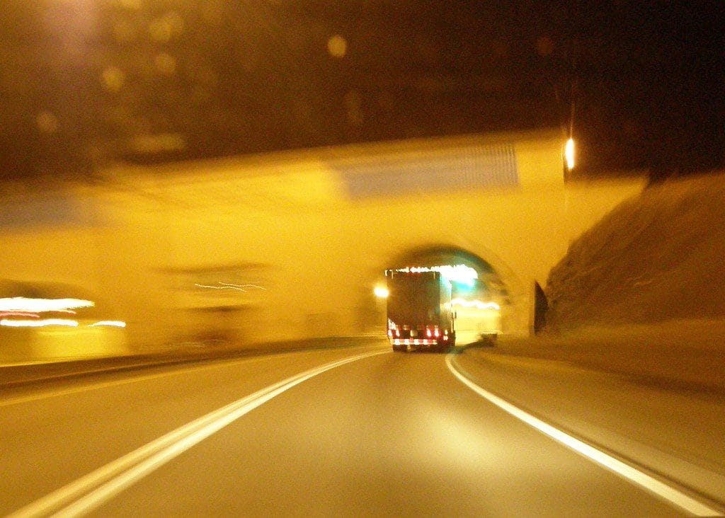 18 wheeler truck going through a tunnel. It is night time and the night lights are yellow. 