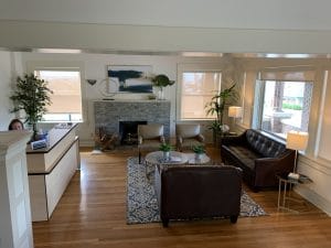 The lobby of The Law Office of Jorge Rivas. There is a fireplace and 1 big sofa, 1 small sofa, 2 chairs and a round glass table in the middle. The round glass table is in the center on a rug on wooden floor. 