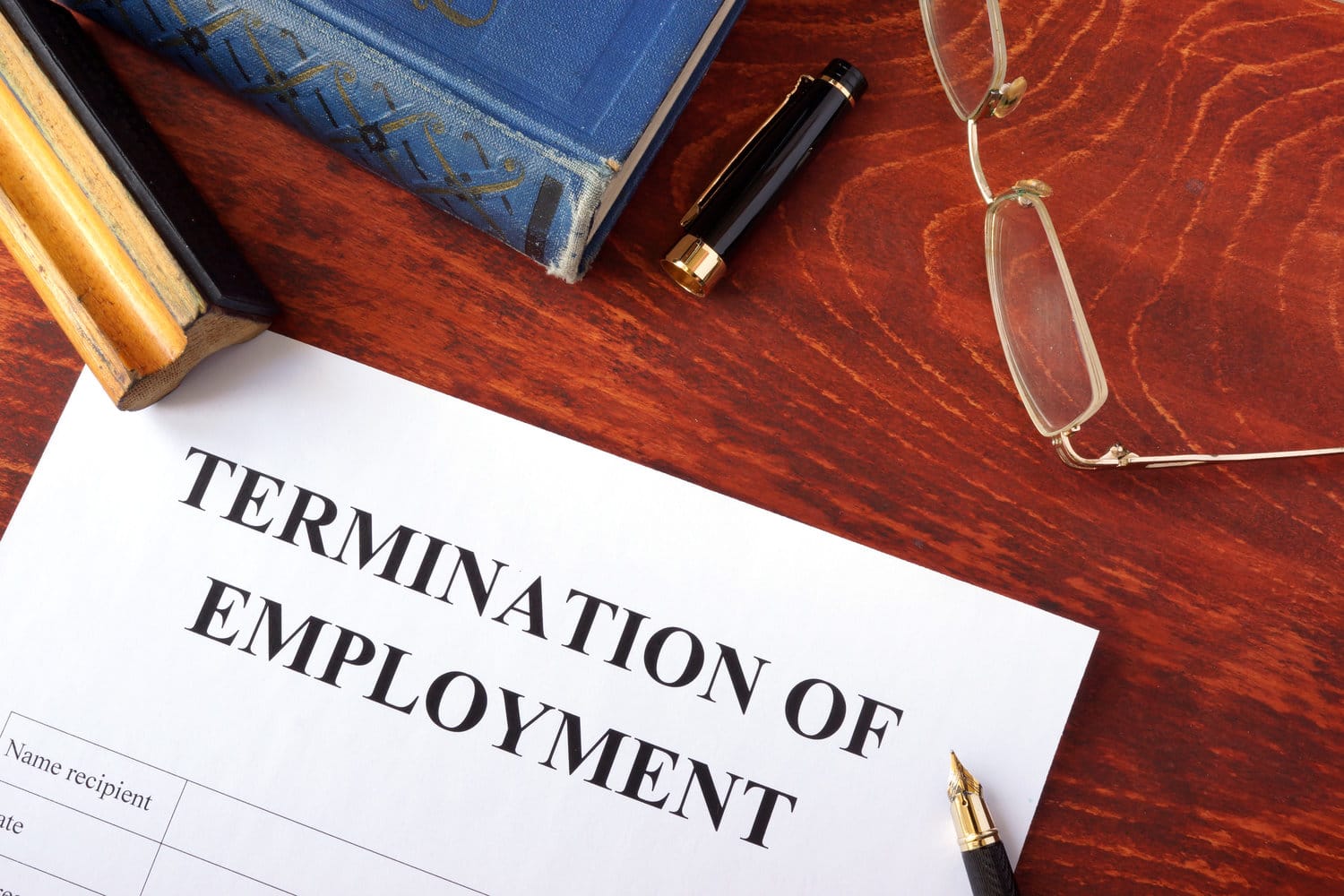 A termination of employment document on a desk with a pen, book, and glasses.