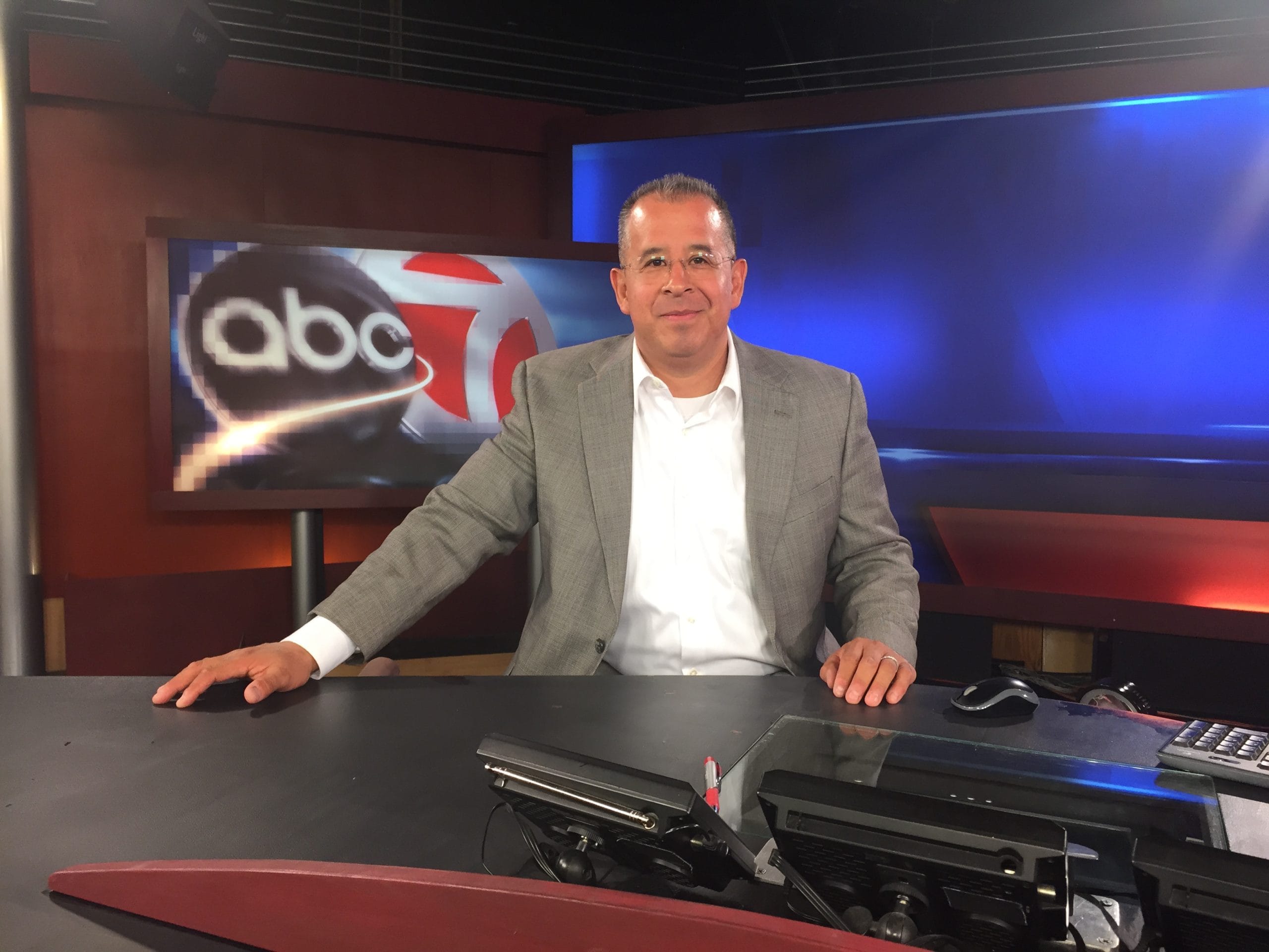 This image shows a man in a studio setting.
He is wearing a blazer and shirt.
There is a desk in front of him.
The background features a television screen with a logo.
KVIA Channel 7 El Paso, Texas