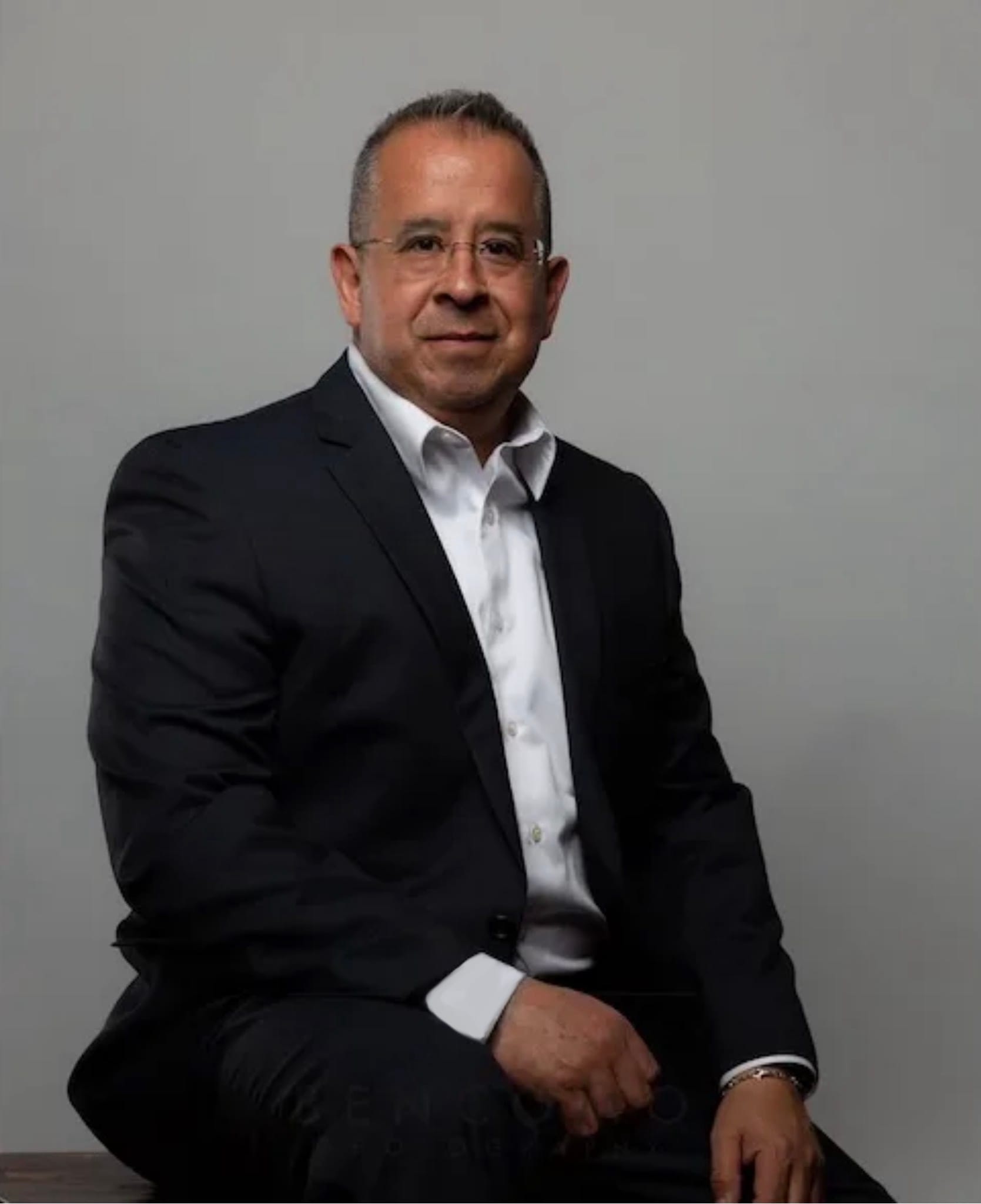 Attorney Jorge Rivas, Jr. sitting in his conference room wearing a blue suit with a light red tie.